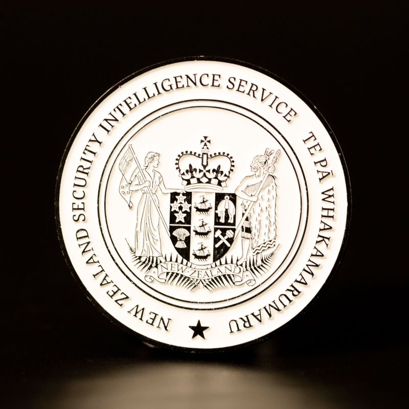 Custom New Zealand Security Intelligence Service challenge coin in a black finish with white enamel fill. The New Zealand coat of arms is in the centre.