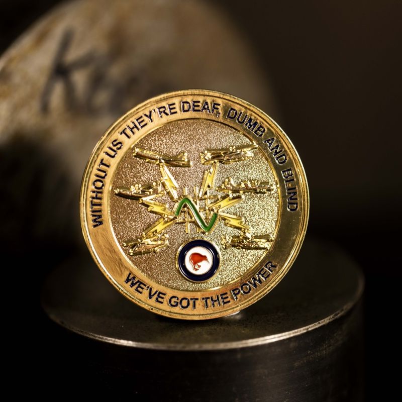 Custom Royal New Zealand Army 'Logistic Regiment' challenge coin in antique gold finish, with the unit's logo in the centre. The logo is coloured with enamel. The edge of the coin has oblique lines.