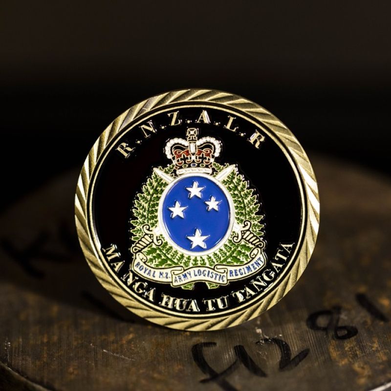 Custom Royal New Zealand Army 'Logistic Regiment' challenge coin in antique gold finish, with the unit's logo in the centre. The logo is coloured with enamel. The edge of the coin has oblique lines.