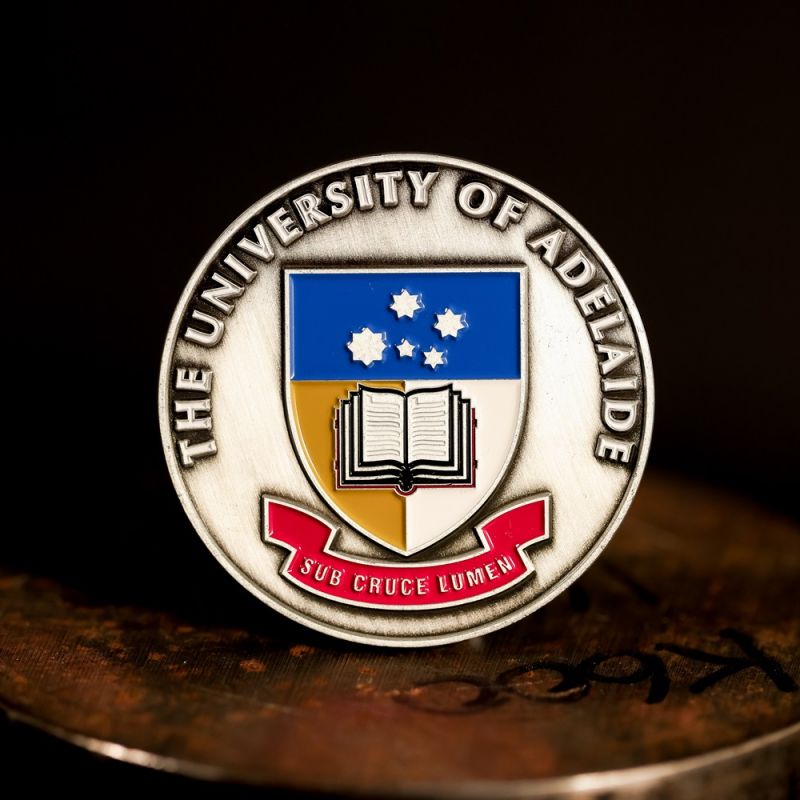Custom University Of Adelaide challenge coin in antique silver finish, with a custom design in the centre. The logo is coloured with enamel. 