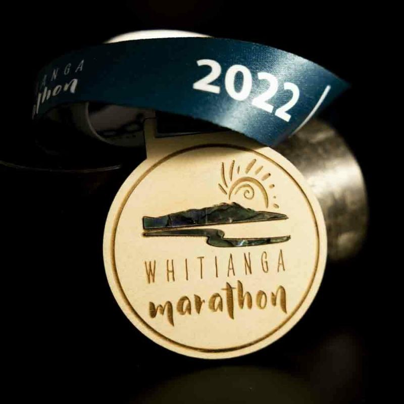 Wooden Whitianga Marathon custom event medal. The event's logo is laser engraved onto the wood. The medal features custom paua shell detailing.
