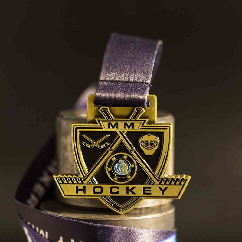 Metal MM Hockey custom event medal with an antique gold finish. The event's logo is coloured in with enamel. The medal is a custom shape.