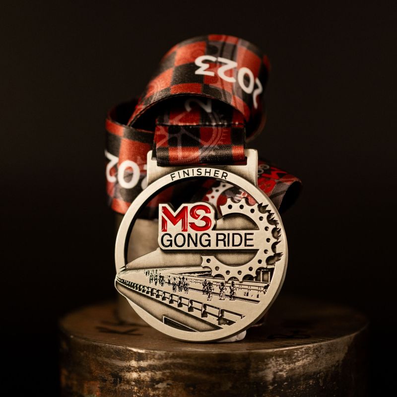 Metal multiple sclerosis Gong Ride custom event medal with an antique silver finish. The medal features a decorative cut out. The event's logo is coloured in with enamel. 