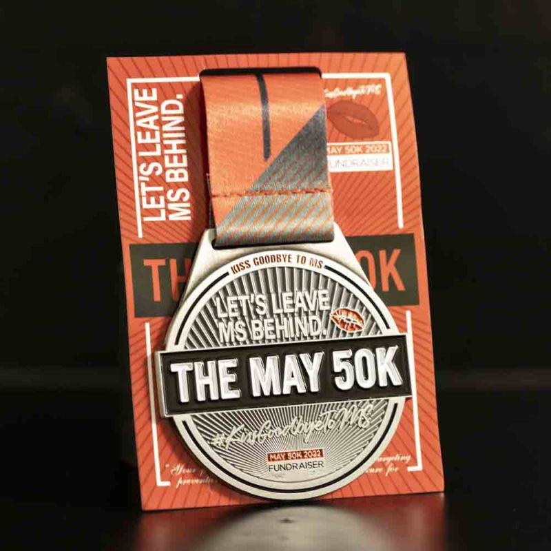 Metal The May 50K custom event medal with an antique silver finish. The event's logo is coloured in with enamel. The medal comes with a backing card. 