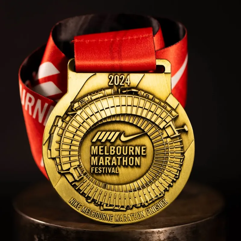 Metal Nike Melbourne Marathon custom event medal with antique gold finish. The marathon's logo is coloured in with enamel. The medal features a cut out that doubles as a bottle opener in its centre. 