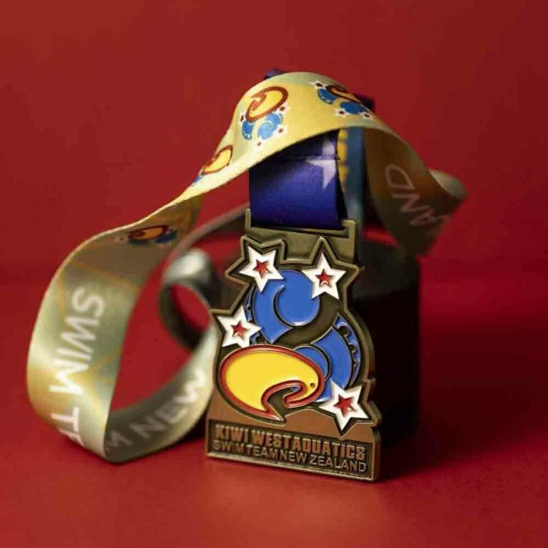 Metal Kiwi West Aquatics custom event medal with an antique gold finish. The event's logo is coloured in with enamel. The medal is a custom shape.